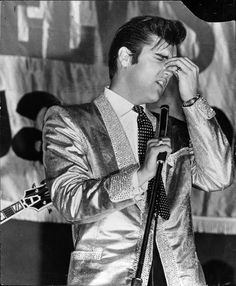 elvis presley singing into a microphone while holding his hands up to his face in front of him