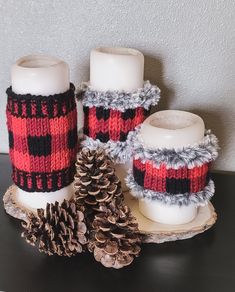 three knitted candles sitting on top of a wooden table next to two pine cones