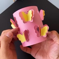 a hand holding a pink paper cup with yellow butterflies on it, and another person's hands