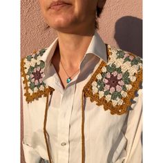 a woman wearing a white shirt with crochet on the chest and collar is standing in front of a pink wall