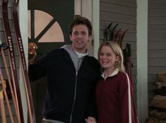 a man and woman standing next to each other in front of a door holding skis