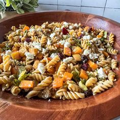 a wooden bowl filled with pasta salad on top of a table