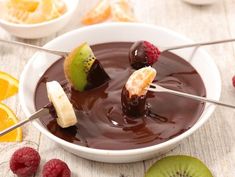 a bowl filled with chocolate and fruit on top of a wooden table next to sliced kiwis