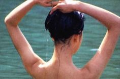 a woman standing in the water with her back to the camera and holding her hands behind her head