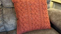 an orange crocheted pillow sitting on top of a gray couch