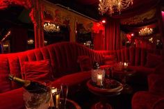 a room with red couches, chandeliers and wine bottles on the tables