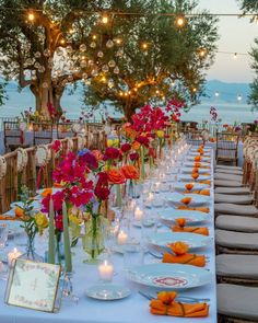 a long table is set up with flowers and candles for an outdoor wedding reception by the water