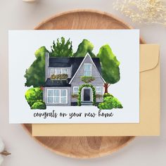 a greeting card featuring a house with flowers and trees on the front, says congrats on your new home