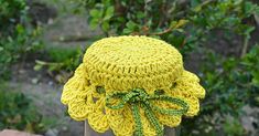 a yellow knitted hat sitting on top of a wooden table next to some bushes