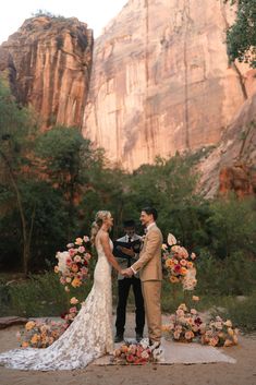 a bride and groom standing next to each other in front of a mountain with flowers