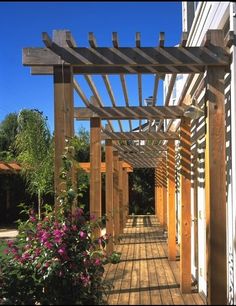 a wooden pergolated walkway next to a building with flowers growing on the side