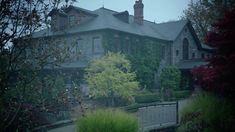 a large house sitting next to a lush green forest on a foggy day in the rain