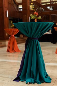 the table is covered with green cloth and has flowers on it, along with other tables