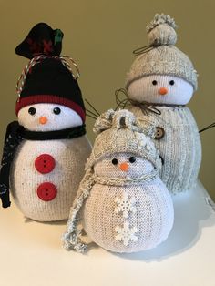 three knitted snowmen sitting next to each other on top of a white table