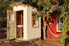 an outhouse is built into the side of a tree in front of a red building