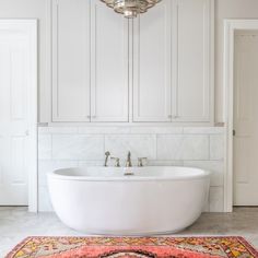 a large white bathtub sitting in the middle of a bathroom next to a rug