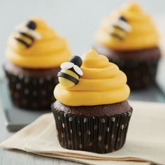 three cupcakes with yellow frosting and bees on top are sitting next to each other