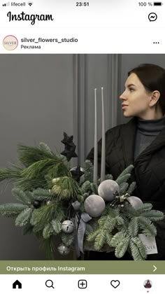 a woman holding a christmas arrangement with candles and greenery in front of her face