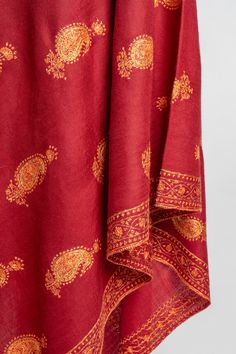 This deep red merino wool shawl features a stunning spread of Sozni hand-embroidered paisleys in golden hues, each pattern meticulously placed to showcase the masterful craftsmanship of Kashmiri artisans. The balanced use of intricate motifs against the bold red fabric lends an air of classic charm to the piece. Perfect for special occasions or as a statement wrap on chilly evenings, this shawl adds both warmth and sophistication to your look. The luxurious feel and exceptional embroidery make i Traditional Patterned Scarves For Eid, Festive Scarves With Intricate Embroidery In Traditional Drape, Festive Scarves With Intricate Embroidery And Traditional Drape, Festive Jamawar Scarves With Intricate Embroidery, Elegant Red Shawl With Traditional Drape, Elegant Red Scarf For Festive Season, Elegant Red Festive Scarf, Transitional Pashmina Shawl With Zari Work, Red Pashmina Shawl With Pallu