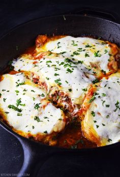 an iron skillet filled with cheese covered ravioli and meatballs, garnished with parsley