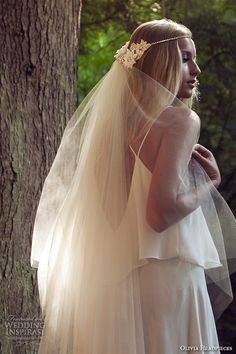 a woman in a wedding dress standing next to a tree wearing a bridal veil