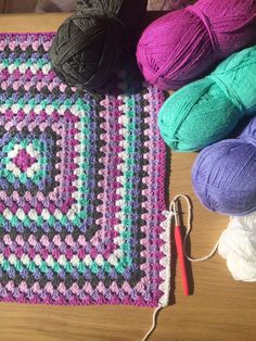 balls of yarn sit on top of a crocheted rug next to two skeins of yarn