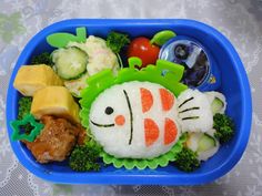 a bento box filled with rice, vegetables and meats in the shape of fish