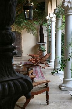 a row of chairs sitting on top of a patio next to tall pillars and potted plants