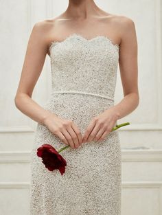 a woman in a white dress holding a red flower with her hands on the waist