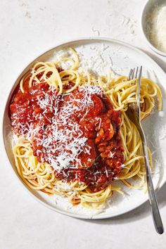 a plate of spaghetti with sauce and parmesan cheese on the side next to a fork