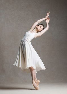 a woman in a white dress and ballet shoes is doing an acrobatic pose