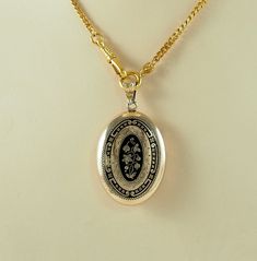 A charming antique Victorian oval gold filled and black enamel sentimental or mourning locket back pendant, in a yellow gold tone. The front with a bleeding heart flower in full bloom with two further buds and foliage, in gilt on a black ground, with a border of scrolls and tiny flower heads.  With an opening machine engraved panel to the reverse with space within for hair or a keepsake, with both frames and one glass. Unmarked. The chain is for display only. Germany 1880s.  8g The opening panel Victorian Yellow Gold Pendant Locket Necklace, Victorian Yellow Gold Locket Necklace, Victorian Style Yellow Gold Locket Necklace, Vintage Necklace With Engraving Option For Keepsake, Victorian Yellow Gold Locket Jewelry, Vintage Oval Jewelry With Engraving Option, Vintage Oval Jewelry With Black Enamel, Vintage Oval Black Enamel Jewelry, Elegant Black Jewelry With Engraving Option