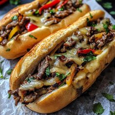 two sandwiches with meat, cheese and peppers on them sitting on top of wax paper