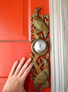 a person is holding the door handle on a red door with an ornate metal latch