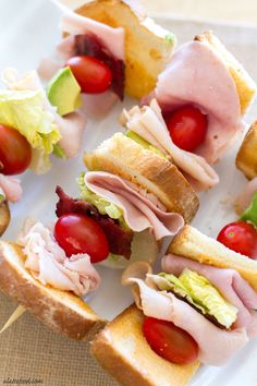 many different types of sandwiches on a white plate with tomatoes, lettuce and meat