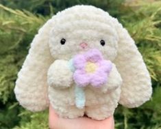 a hand holding a small stuffed animal with a flower in it's mouth,