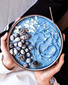 a person holding a bowl with blue frosting and berries