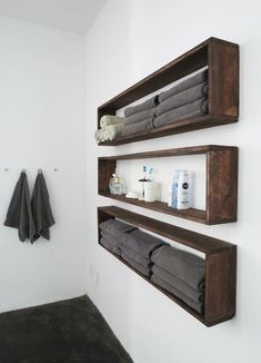 two wooden shelves with towels on them in a white walled bathroom, along with other items