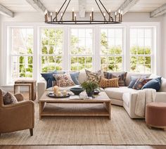 a living room filled with lots of furniture next to two large windows and a chandelier hanging from the ceiling