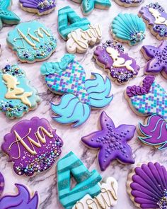 decorated cookies are displayed on a table with purple, blue and white icing in the shape of mermaids