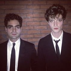 two young men in suits and ties standing next to each other against a brick wall