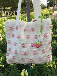 a crocheted bag with strawberries on it hanging from a pole in the grass