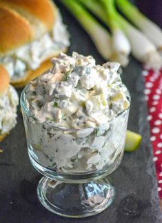 a glass bowl filled with chicken salad next to buns and celery sticks