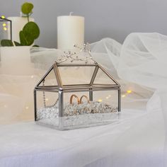 two wedding rings in a glass box on a white tablecloth with candles and flowers