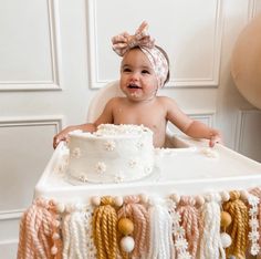 a baby sitting in a high chair next to a cake