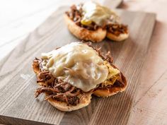 two pulled pork sandwiches with gravy on a wooden cutting board