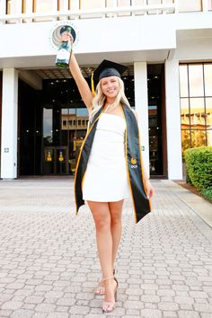 a woman wearing a graduation gown and holding up a trophy in front of a building