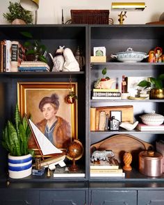 a bookcase filled with lots of books next to a painting and potted plant