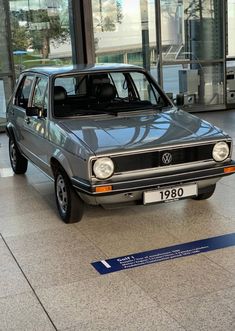 a blue car is parked in front of a glass building with an information board on the floor