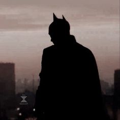 the silhouette of a batman standing in front of a cityscape at sunset or dawn